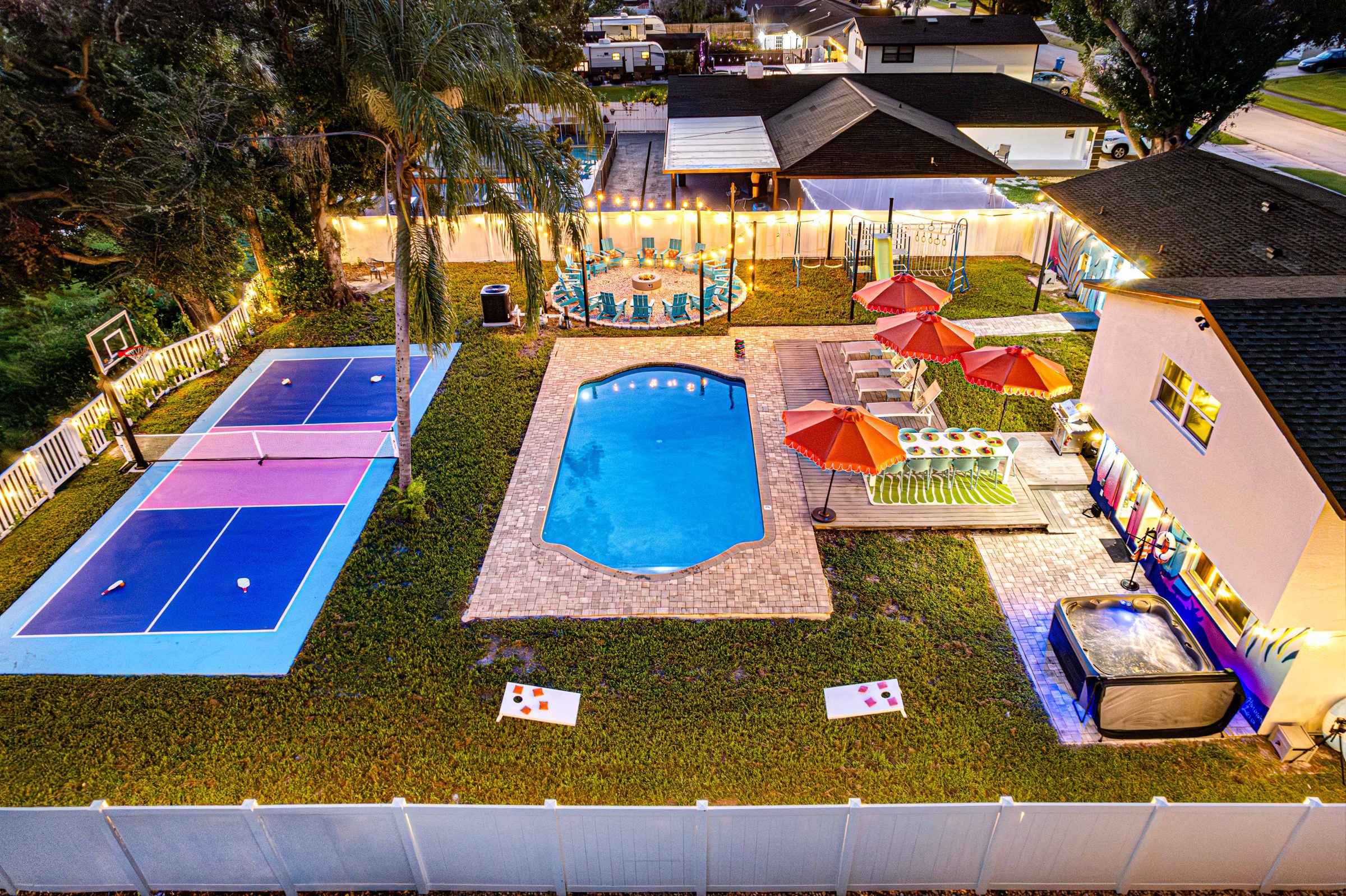 Twilight from above: court, pool, hot tub and fire pit inside one fenced yard