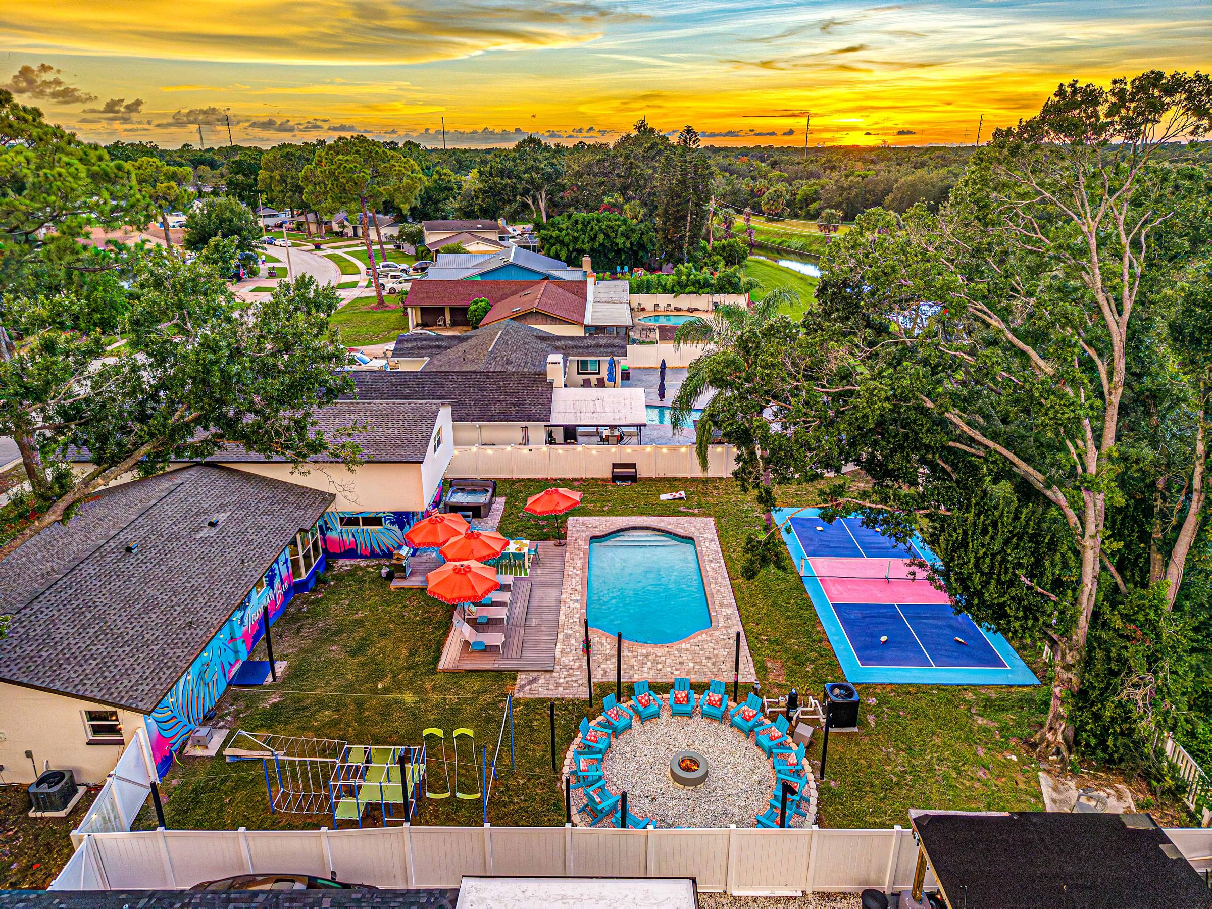Tampa Bae at twilight from above: the pickleball court, heated pool, hot tub and the 16-chair fire pit, all inside one fenced backyard